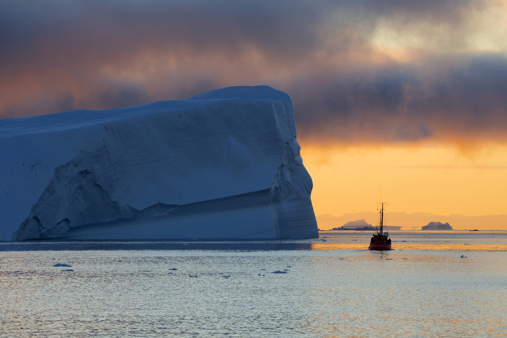 Iceberg dwarfs boat on winter sea