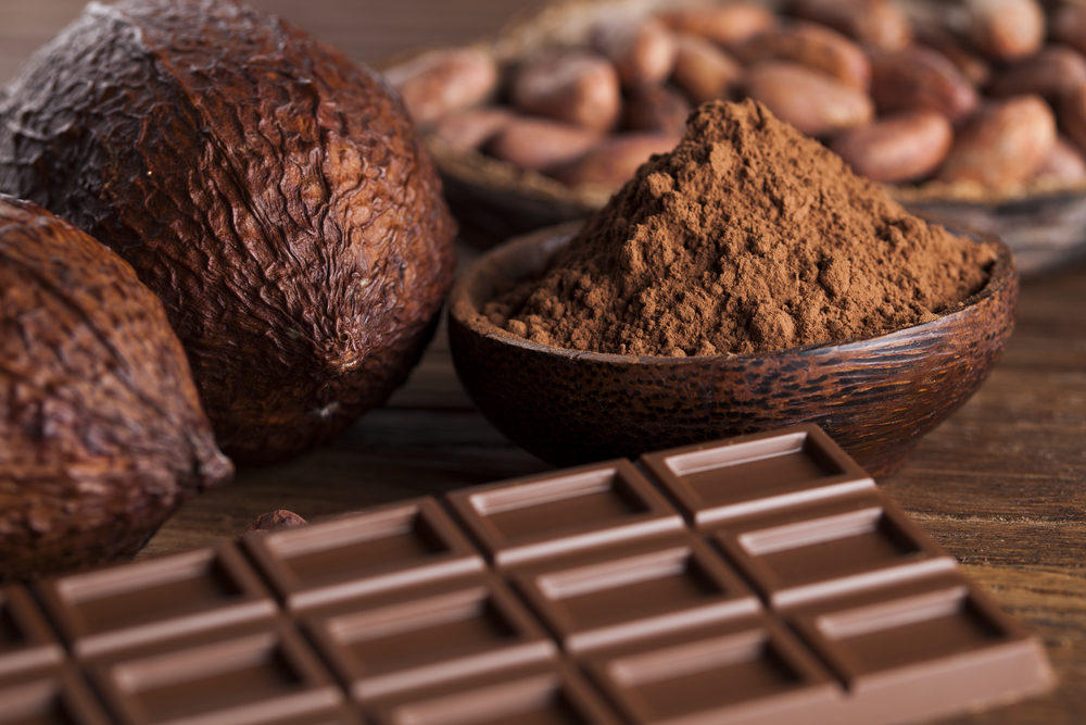 Chocolate bars, cacao pods, beans and a bowl of powder on wooden background