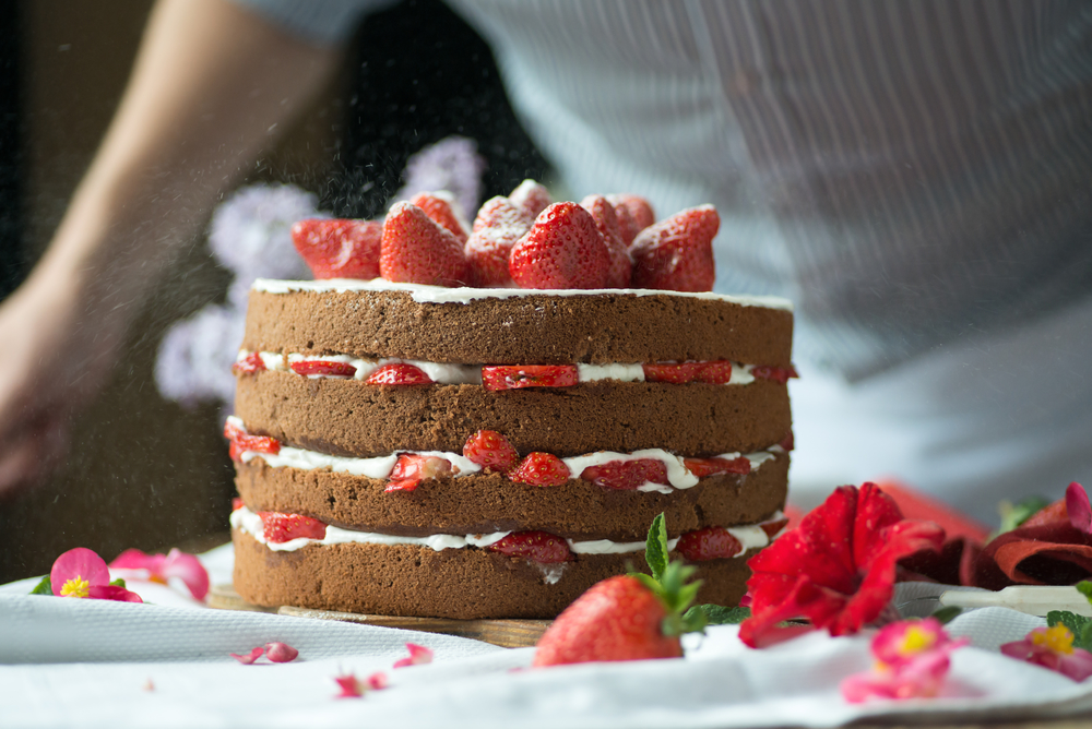 Four layer naked cake with strawberry filling, topped with strawberries and powdered sugar