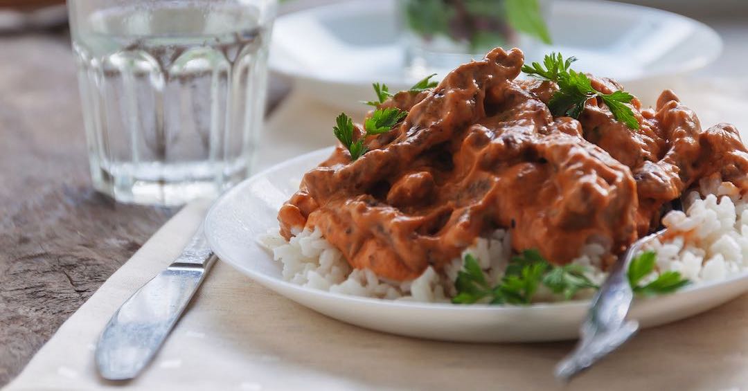 Creamy meat dish over white rice with water and green salad