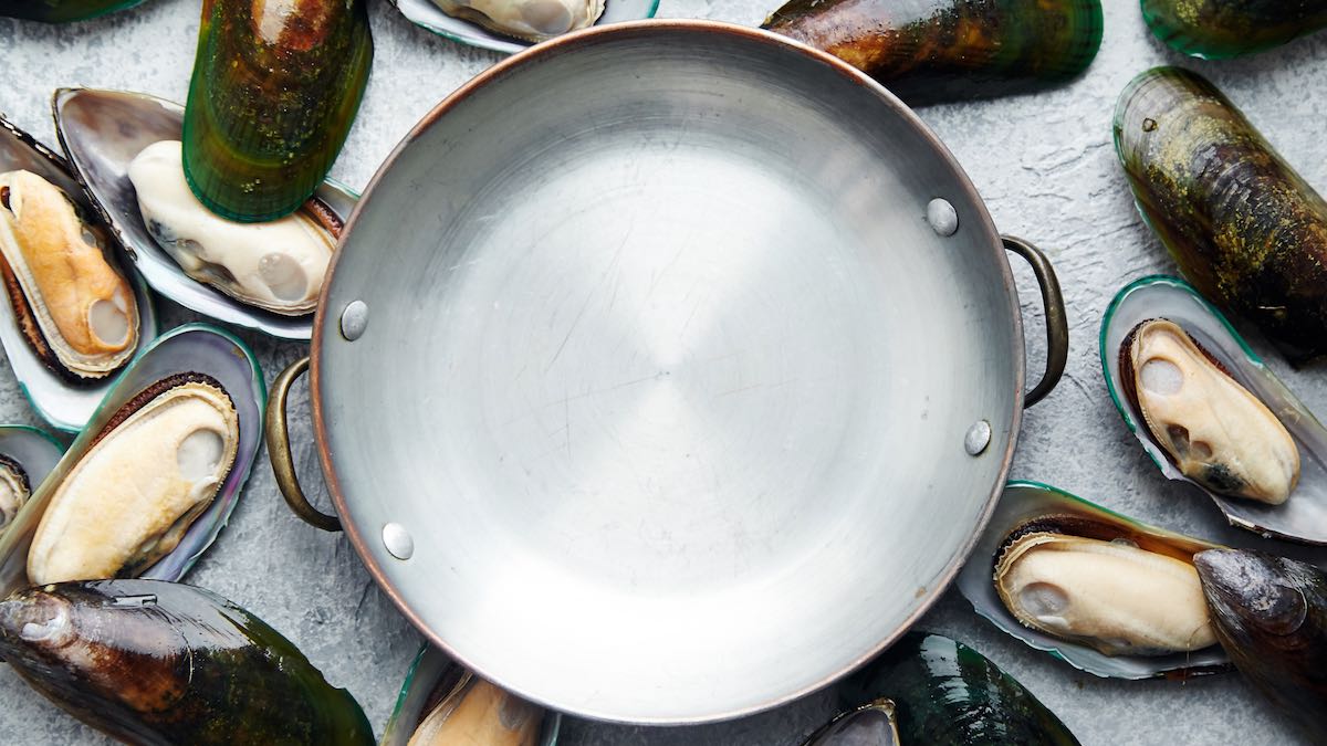 Raw mussels and shells arranged on a rock surface around a metal pan centerpiece