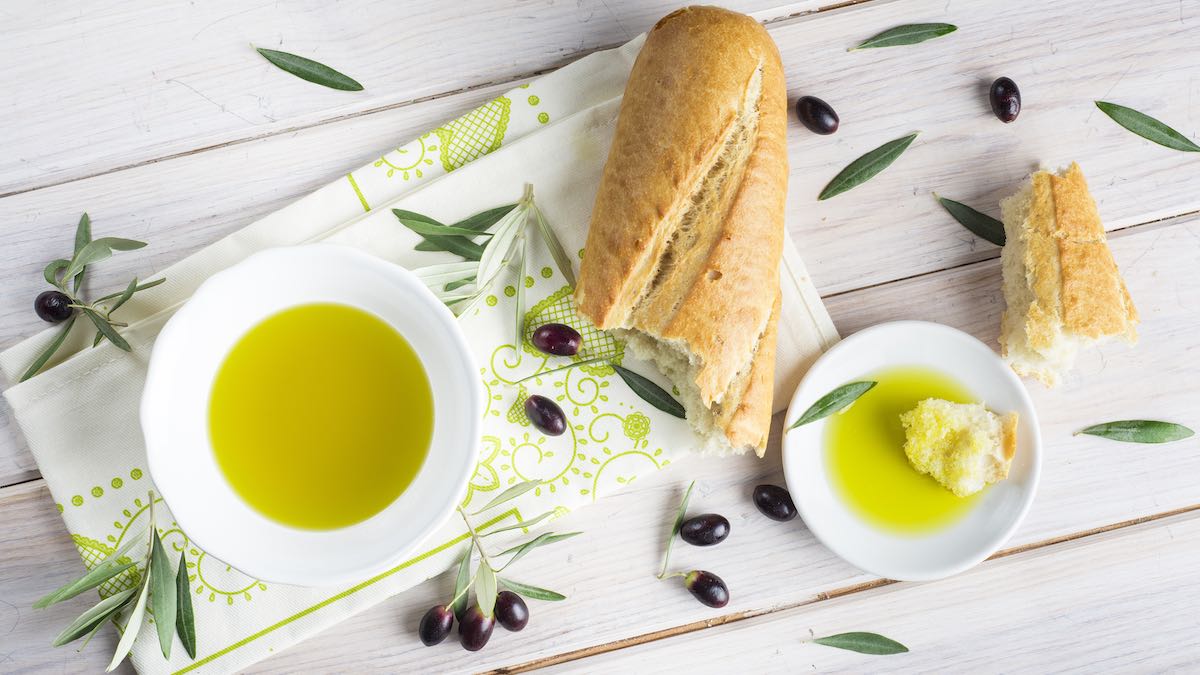 Ripe olives, olive leaves, olive oil dipping saucers and a broken loaf of bread on a table
