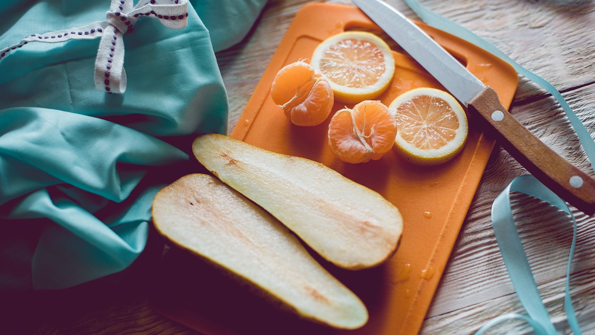 Peeled orange segments, cut lemon sections, sliced pear halves and knife on cutting board
