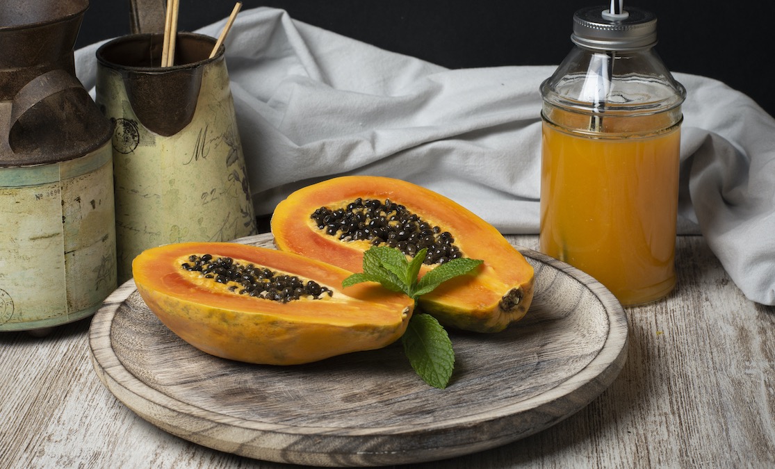 Fresh papaya halves with mint sprig and papaya juice in rustic setting