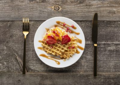Waffles with maple syrup drizzle, sliced strawberries, oranges and pomegranate seeds